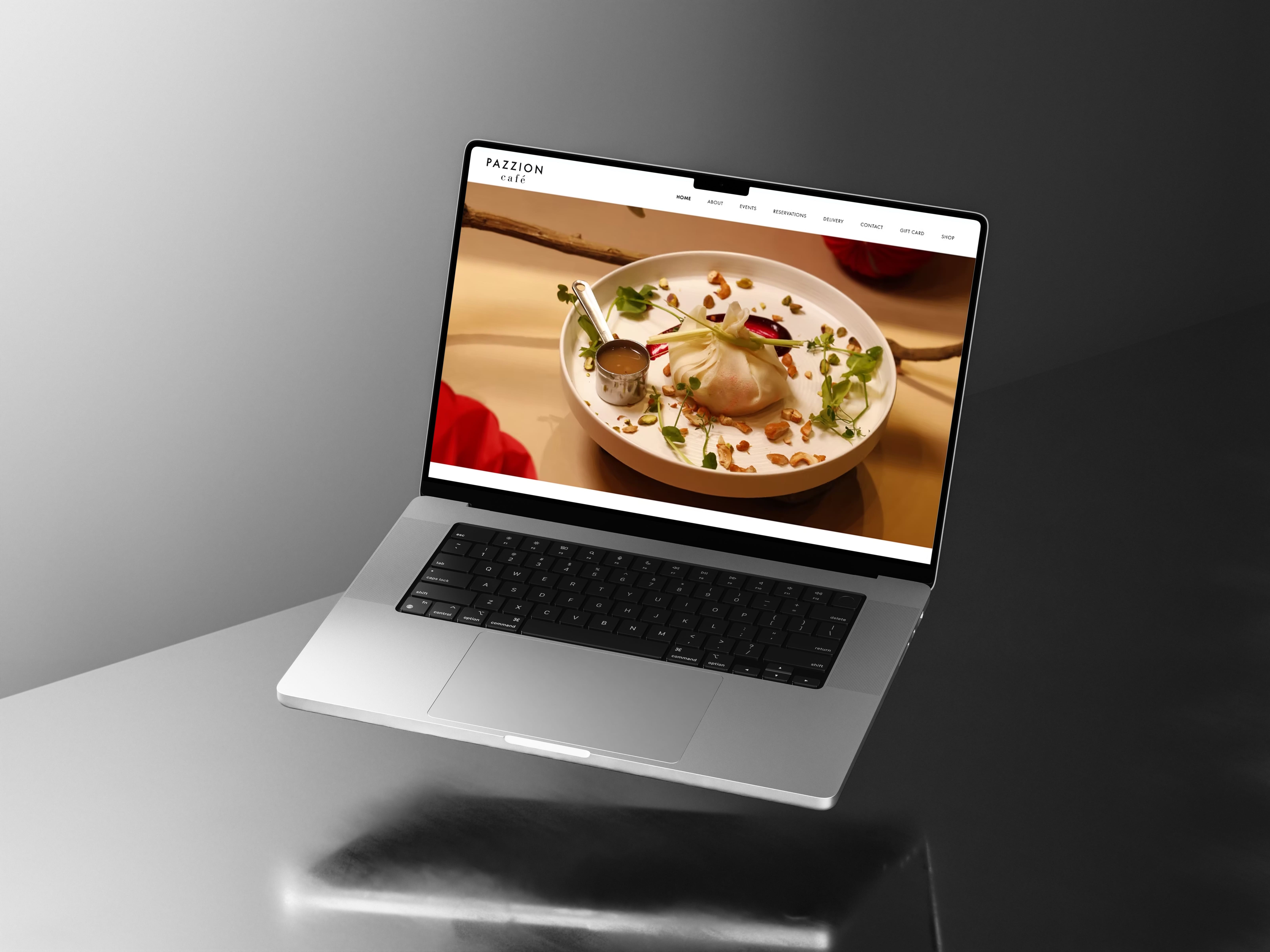 Pazzion Café website homepage on a floating laptop, with the navigation and a plated signature dish hero image